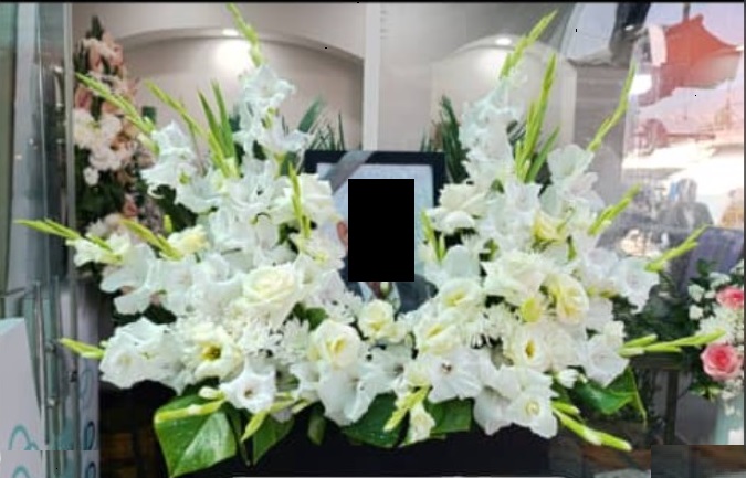 باکس گل تسلیت مشکی با گل‌های گلایول و رز سفید چیده شده به صورت نیم‌دایره دور قاب عکس برای مراسم ختم - سام فلاور.