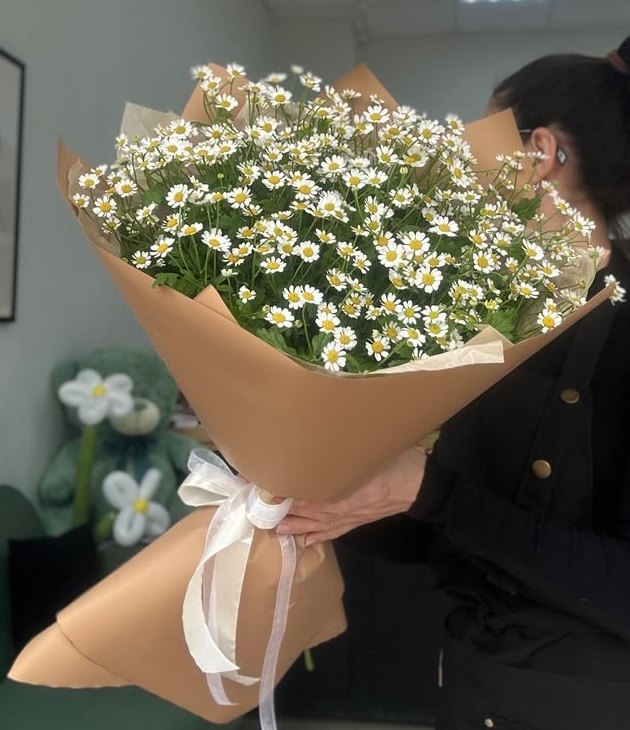 خانم جوانی که دسته گل بسیار بزرگ بابونه با کاغذآرایی قهوه‌ای را در آغوش گرفته است - گلفروشی سام فلاور.