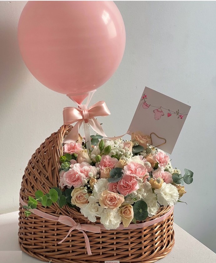 سبد حصیری به شکل گهواره پر از گلهای صورتی و سفید همراه با بادکنک صورتی برای تولد نوزاد دختر - سام فلاور.