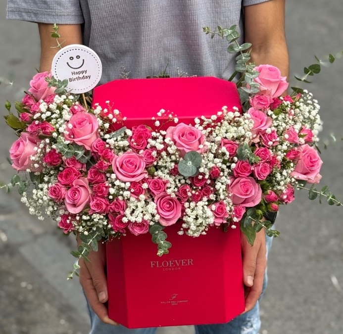 باکس گل شش‌ضلعی به رنگ سرخابی تند با تزئین رزهای صورتی هلندی، گل‌های ریز ژیپسوفیلا و شاخه‌های اکالیپتوس و تاپر Happy Birthday در سام فلاور شاپ.